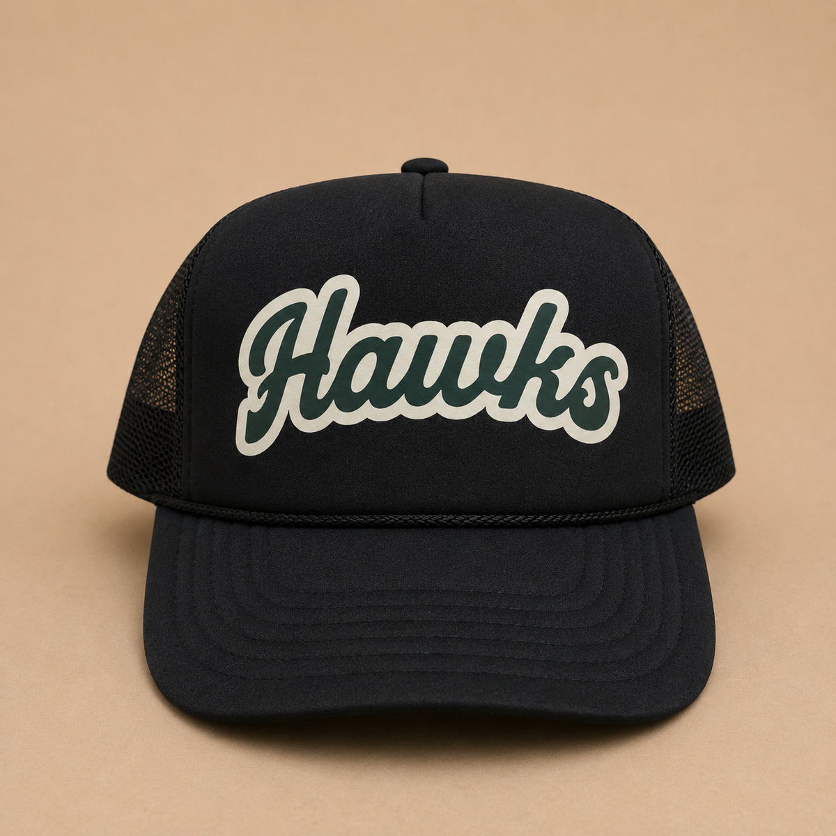 A black trucker-style cap with a curved brim and mesh back panels, featuring the word 'Hawks' embroidered in dark green with a white outline on the front. The cap is photographed against a solid tan background.