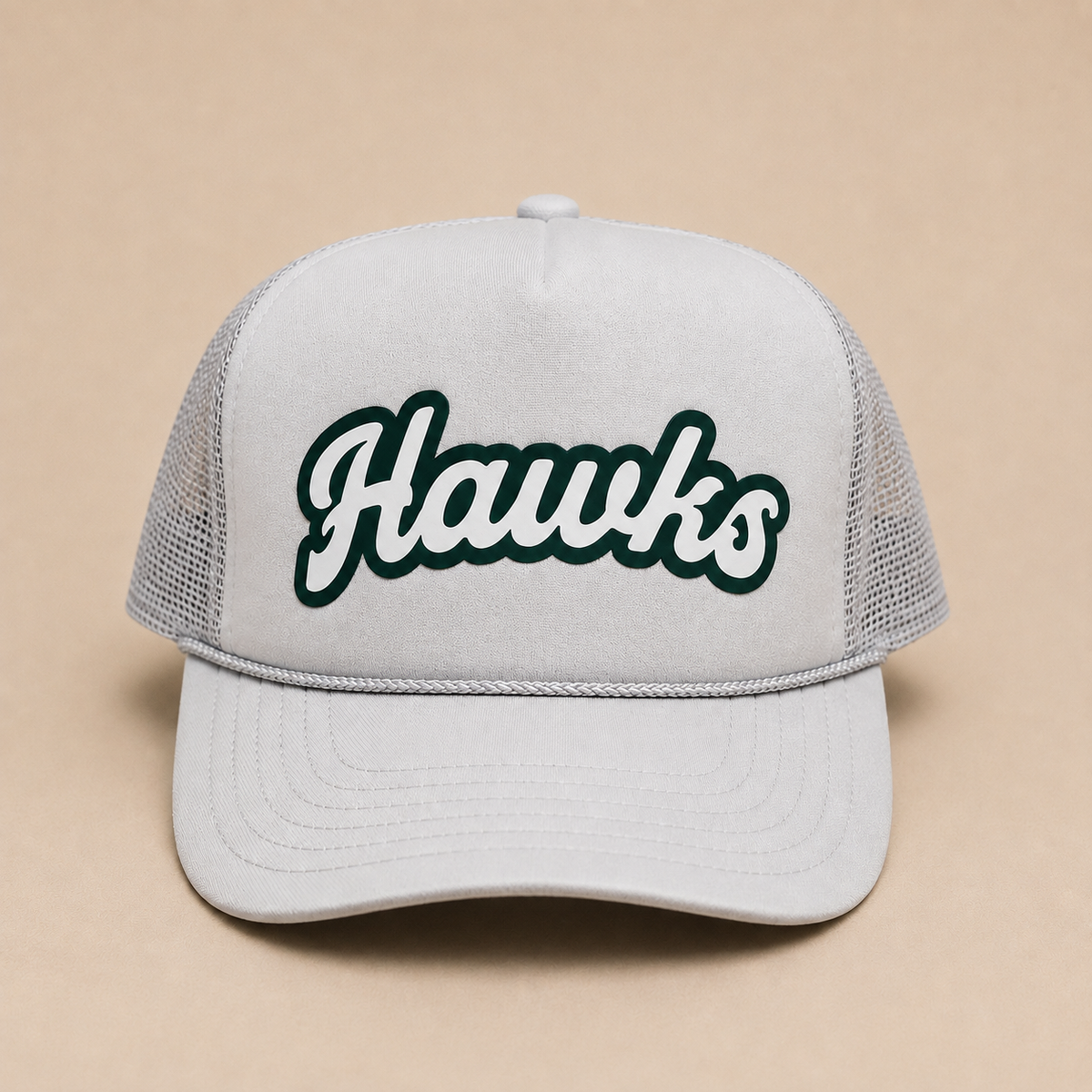 A light gray trucker hat with a curved brim and mesh back, featuring the word 'Hawks' embroidered in white with a dark green outline on the front panel, set against a solid beige background.