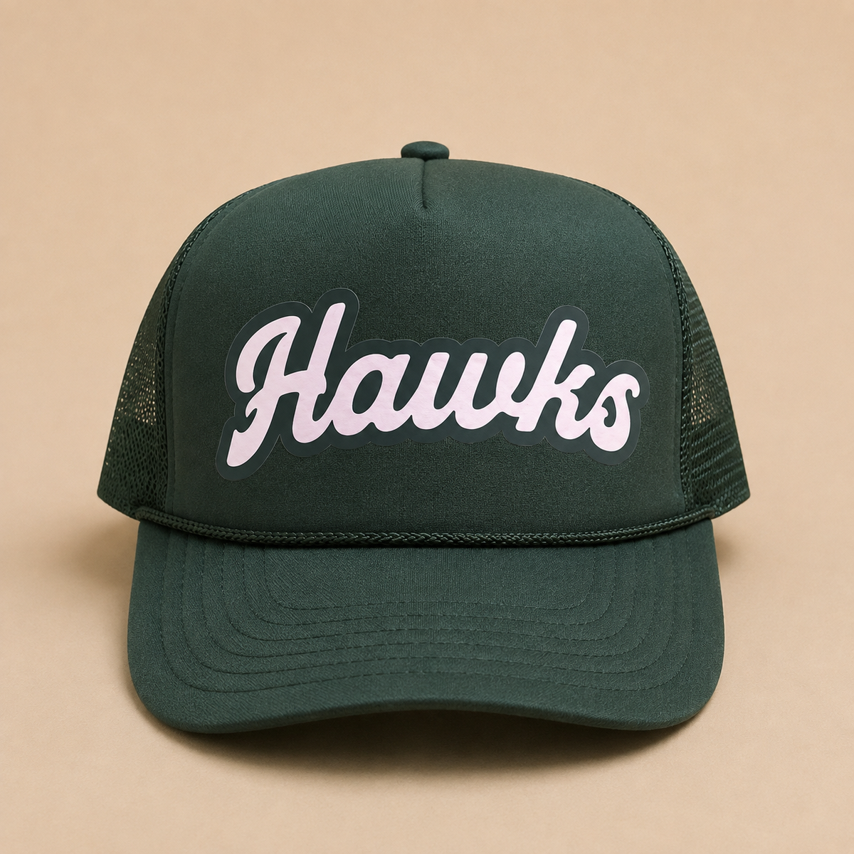 A dark green trucker hat with 'Hawks' embroidered in white script with a black outline on the front, set against a solid beige background.