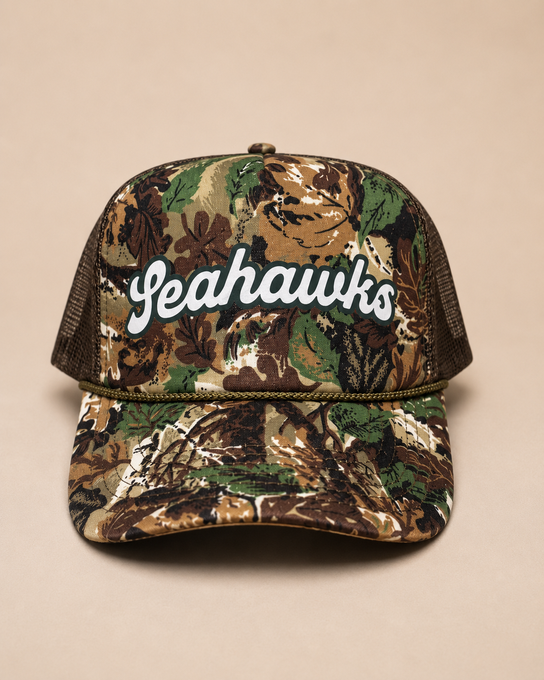 A camouflage trucker hat with a mesh back and 'Yeahawks' written in white script across the front, set against a solid beige background.