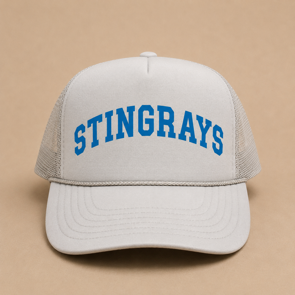 A white trucker hat with 'STINGRAYS' embroidered in blue arched block letters on the front, set against a solid beige background.