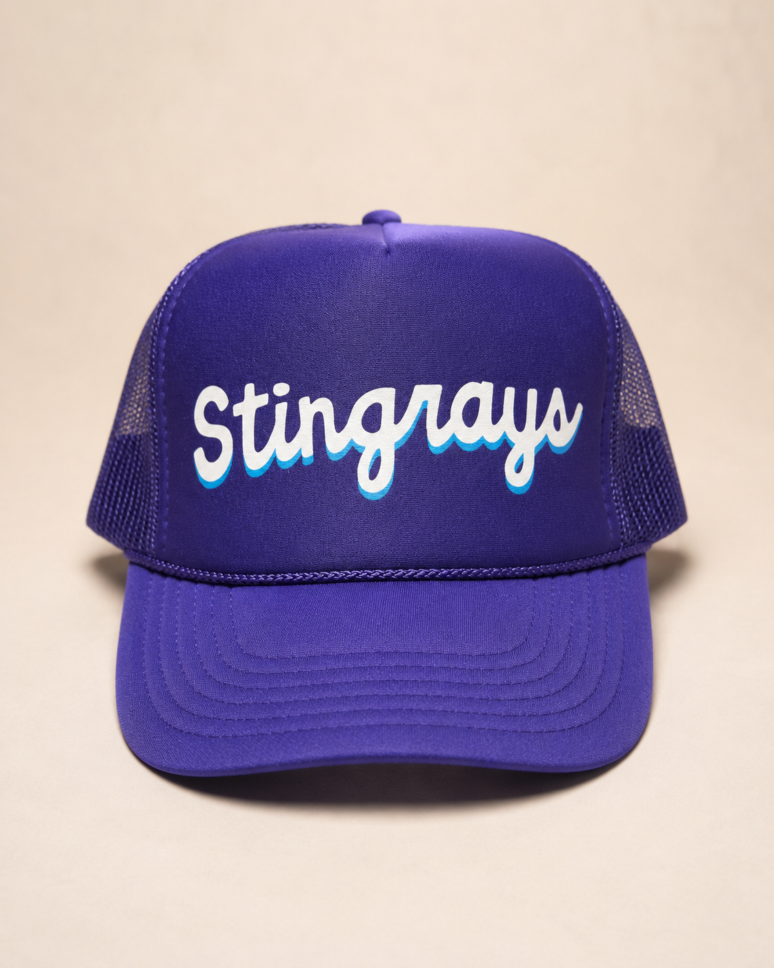 A purple trucker hat with 'Stingrays' embroidered in white script with a light blue shadow effect on the front panel, set against a plain beige background.