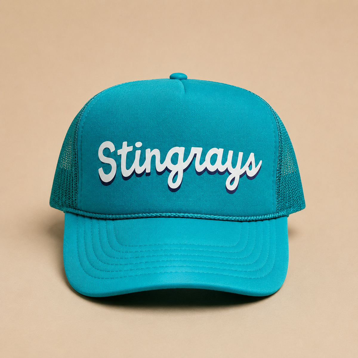 A turquoise blue trucker hat with 'Stingrays' embroidered in white script on the front, set against a solid beige background.